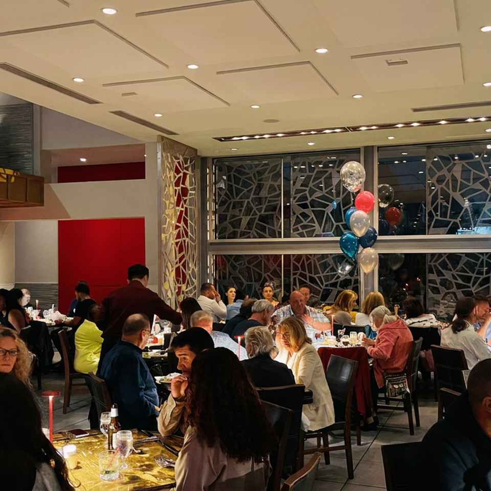 Busy upscale restaurant dining room filled with guests, red accents, patterned windows, and colorful balloon decorations.